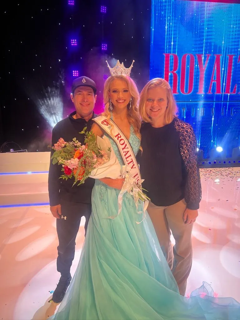 Elle Ables crowned in a teal gown with Susan and Jeremy under a Royalty backdrop