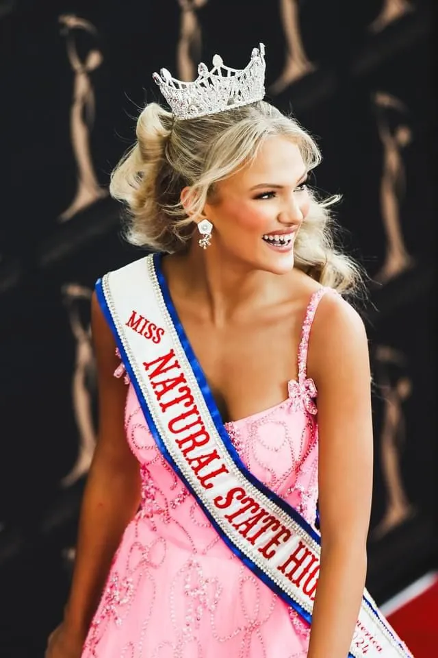 Elle Ables as Miss Natural State High School in a pink gown with a crown and sash