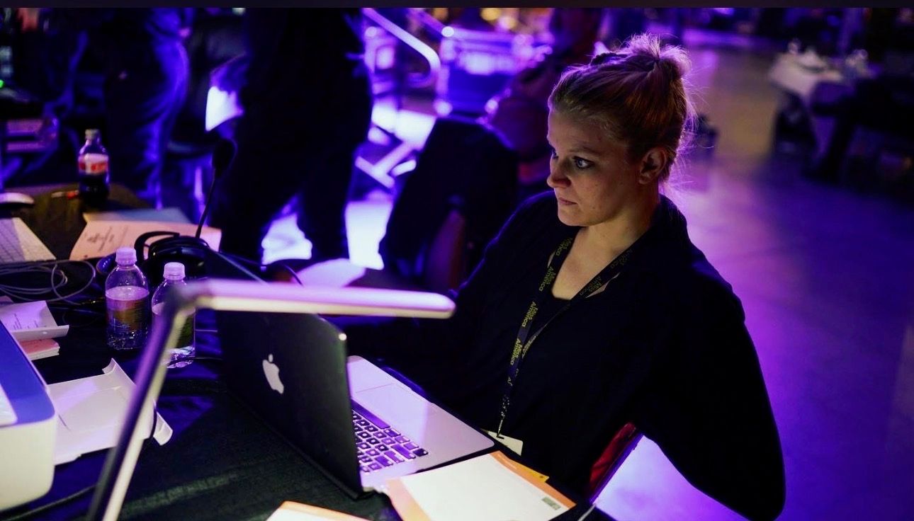Susan working at a production laptop under purple stage lights