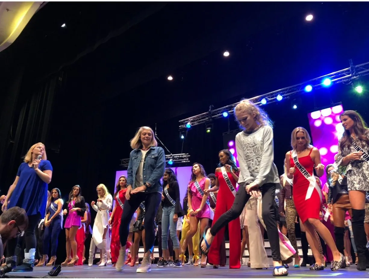 Pageant contestants walking across a stage under colourful lights