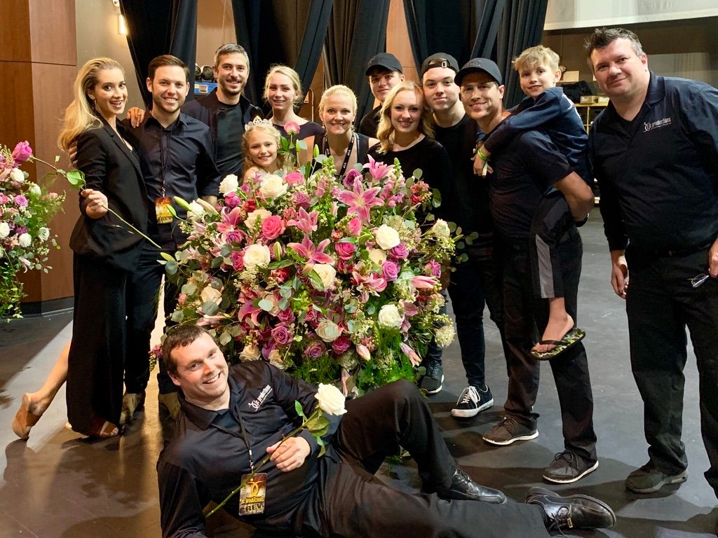 Production crew with contestants beside a floral arrangement
